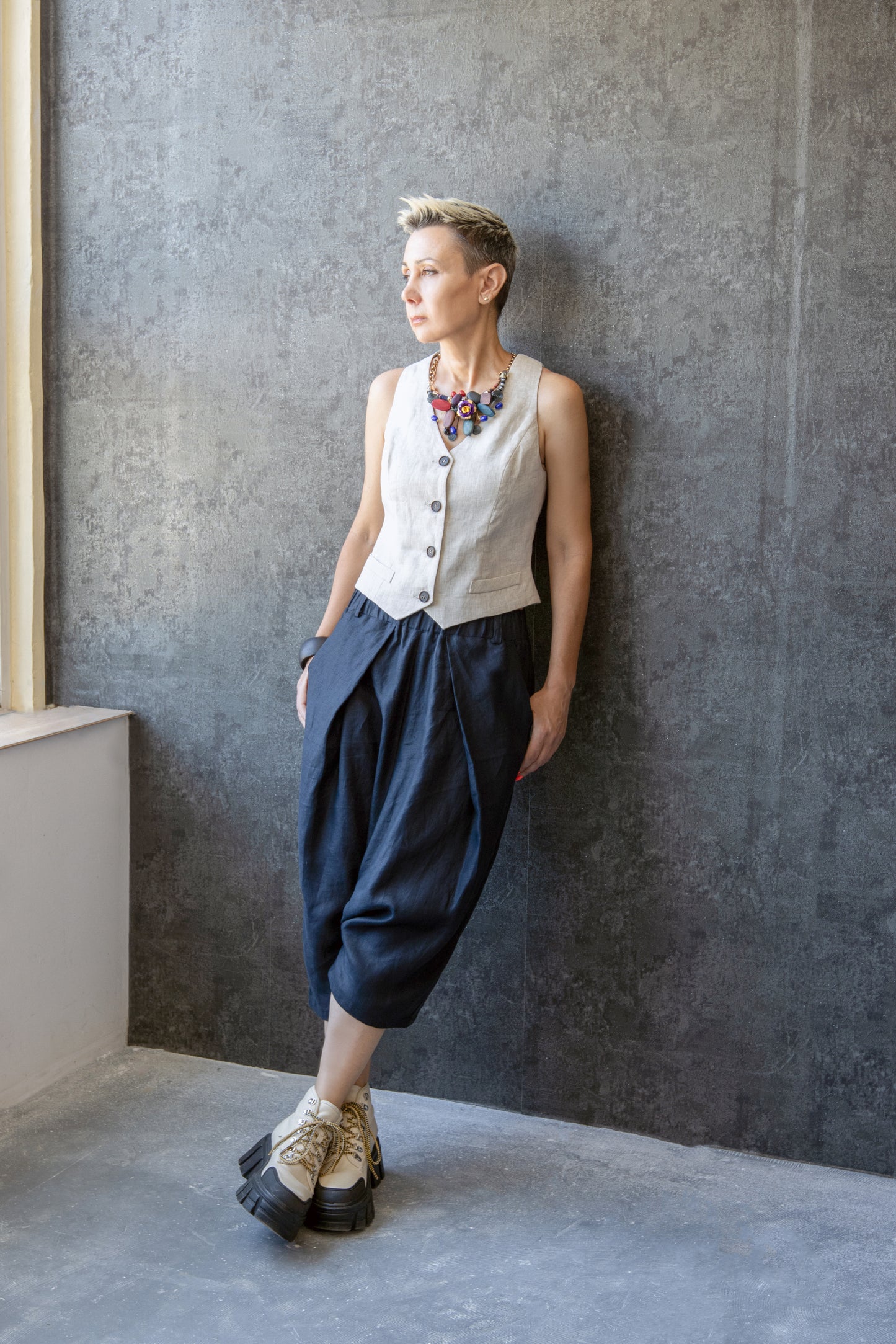 Model wearing linen drop crotch pants with pleats, leaning against textured wall