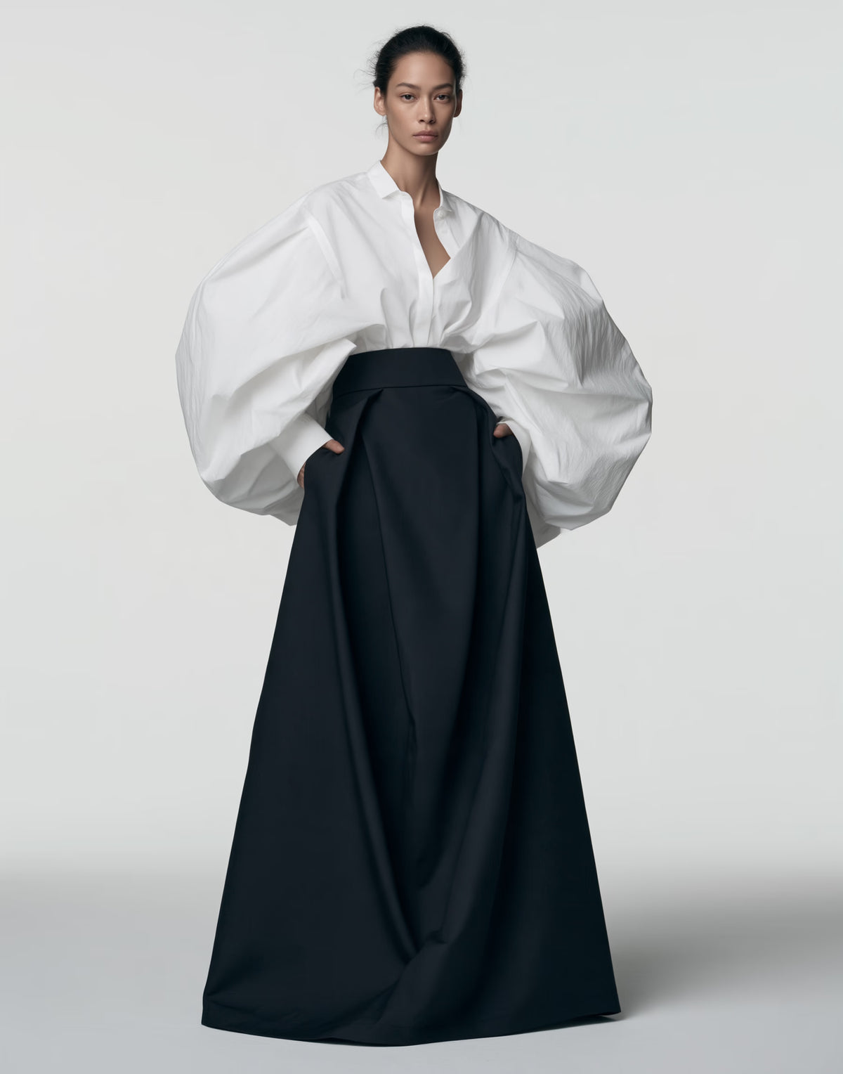 Model wearing a black high-waisted floor-length maxi skirt with a full silhouette, styled with an oversized white blouse.