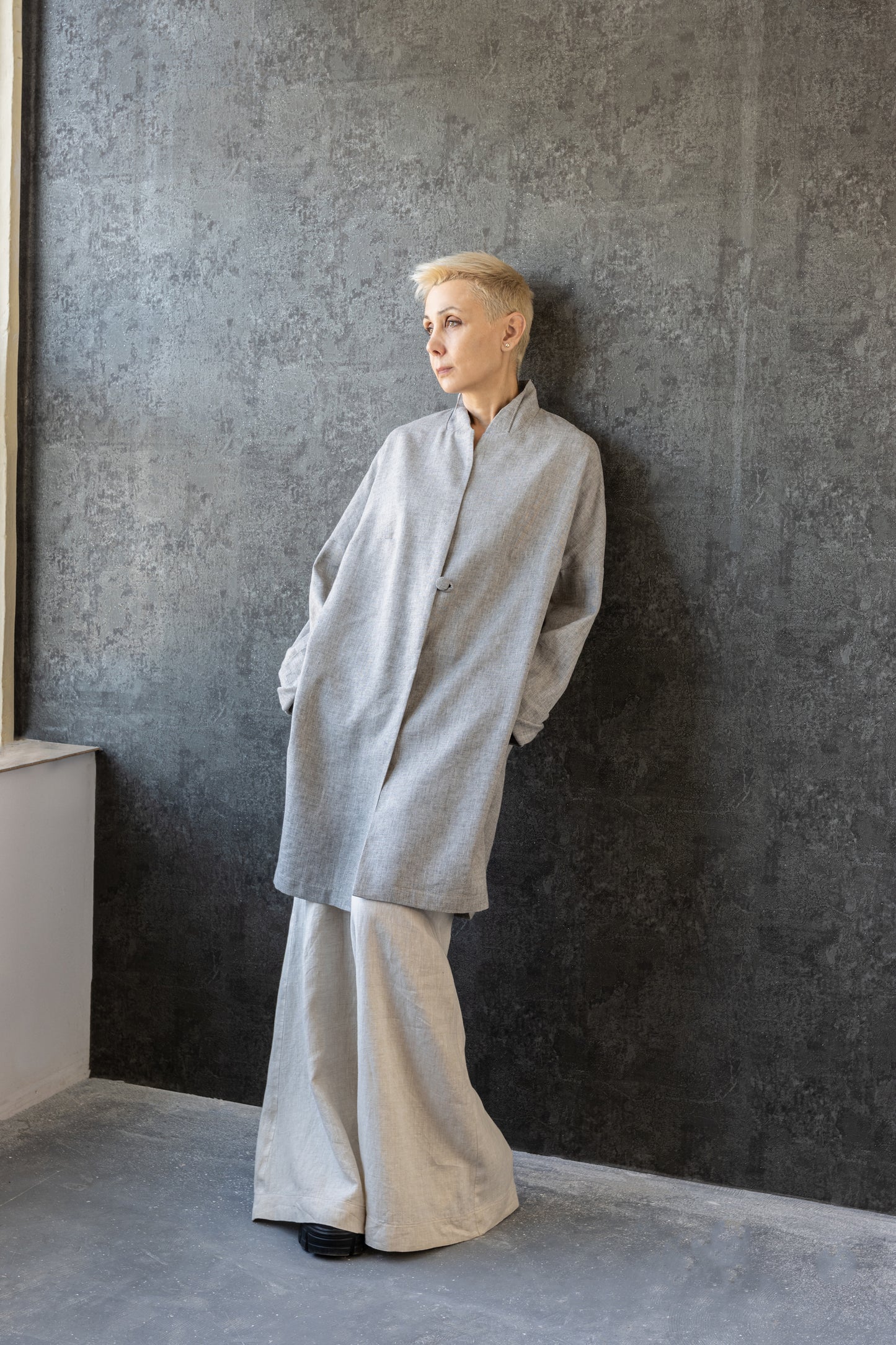 Model wearing the linen summer coat – relaxed styling against grey wall