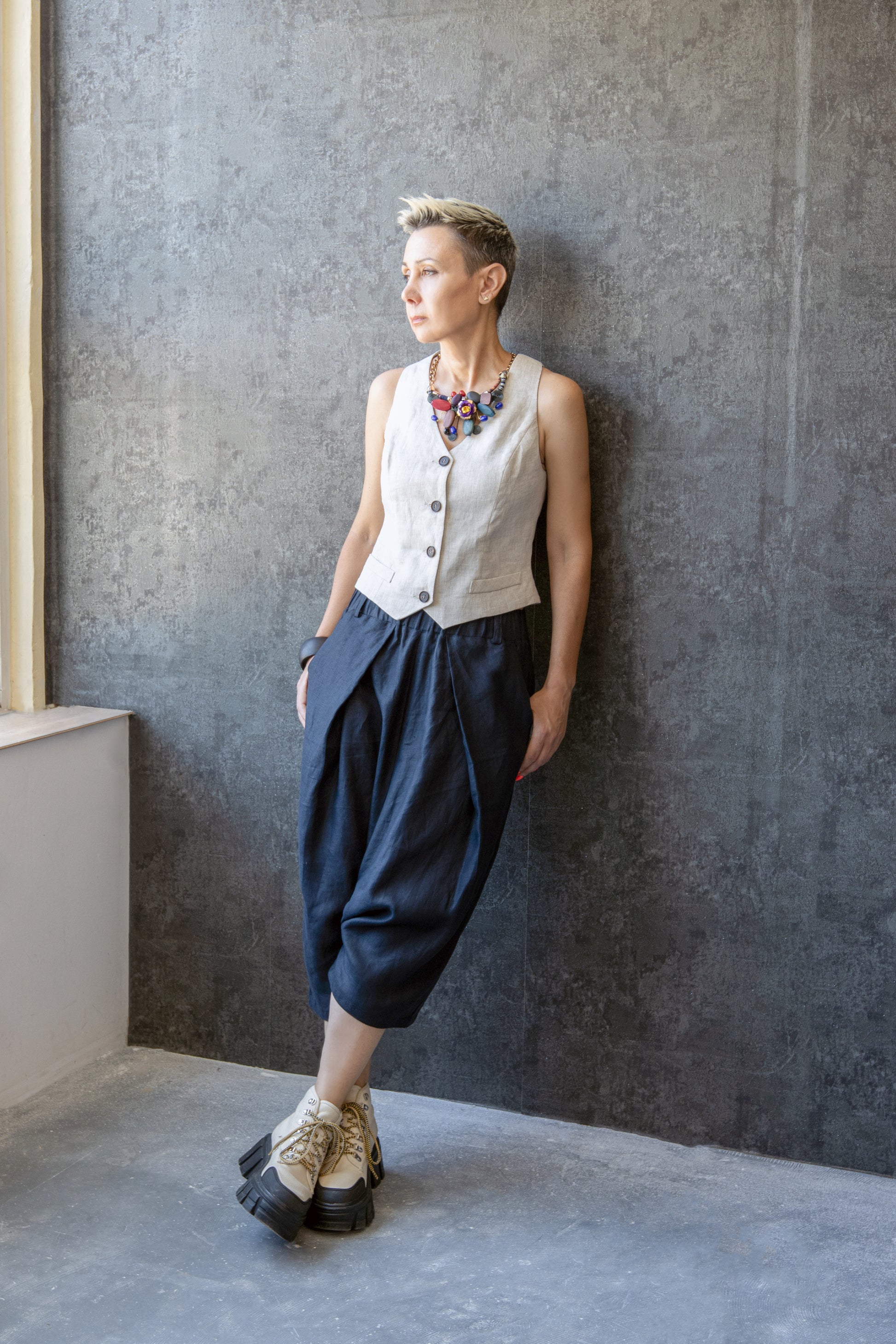 Model wearing linen drop crotch pants with pleats, leaning against textured wall