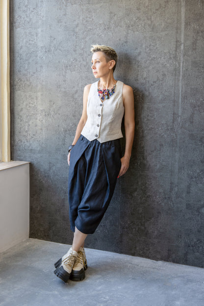 Model wearing linen drop crotch pants with pleats, leaning against textured wall